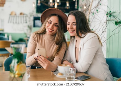 women friends on coffee break at cafeteria using mobile phone