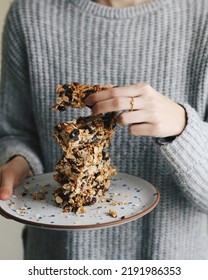 Women In A Grey Sweater Holding A Homemade Almond Honey Granola Bar And A Plate With The Rest Of It