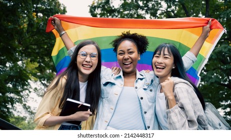 Women Group Enjoying Holding Rainbow LGBT Pride Flag.Smiling Multi Ethnic Female Enjoying Displaying Anti-racism Symbols For LGBT Rights. Diversity,tolerance And Gender Identity Concept.African,Asian.