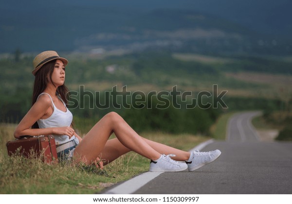 women is hailing a car on a road. Thumbing a ride.\
Outdoors vacation. Asian
