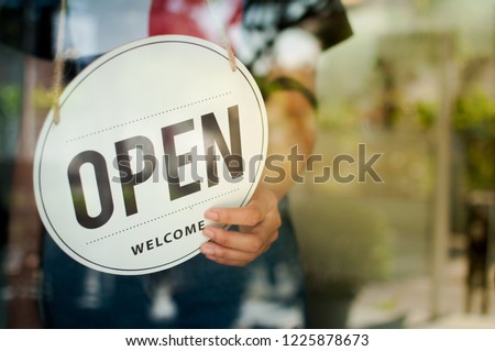 Women hand flip the sign to open the shop. Open sign hanging on the glass door.