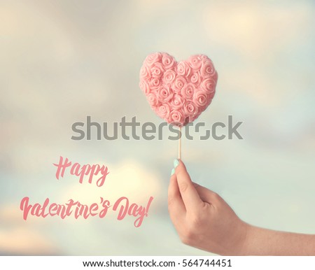 Women hand holding heart lollipop on the sky background. Valentine's Day greeting card.