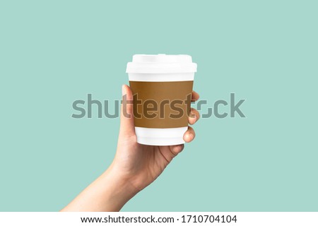 women hand holding mockup paper coffee cup on pastel green background