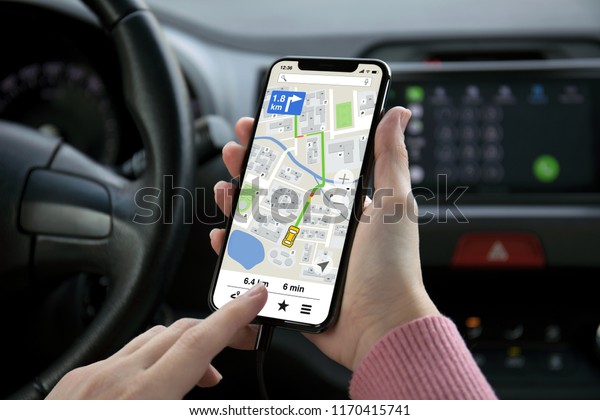 women hand holding phone with app navigation map on\
screen in the car