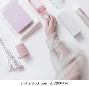 Frauen tragen eine rosafarbene Kosmetikflasche auf modernem Schönheitshintergrund mit Packungen, Kerzen und Blumen. Draufsicht. Pastellfarben
