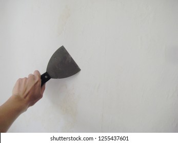 Women Hand Holding Putty Knife Patching A Hole In White Wall. Renovation And Repair Process Indoors, Girl Remodeling Interior Of The Room At Apartment Building