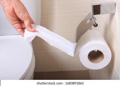 women hand picking napkin/tissue paper from the tissue roll in toilet room.