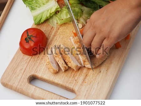 A women hand slices grilled chicken breast with green oak and red tomato on the wooden tray.