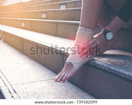 Women hand touching injured ankle, barefoot resting on stair outdoor.  Ankle inflammation, pain.