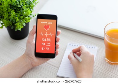 Women hands holding phone with app for health card monitoring and writing in a notebook - Powered by Shutterstock