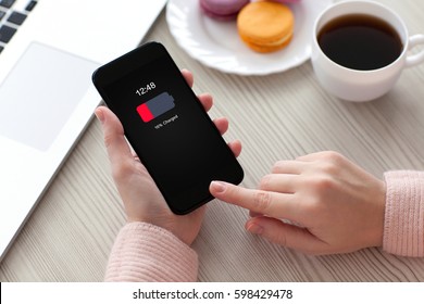 Women hands holding phone with low charged battery screen on table coffee and laptop