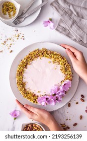 Women Hands Holding A Pink Cheesecake Top View With Some Crushed Pistachios Around And Flowers