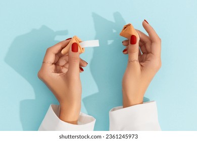 Women hands with manicure holding fortune cookie on blue background. Blank paper for prediction words