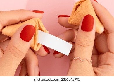 Women hands with manicure holding fortune cookie on pink background