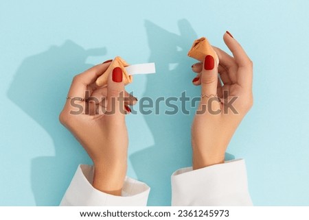 Women hands with manicure holding fortune cookie on blue background. Blank paper for prediction words