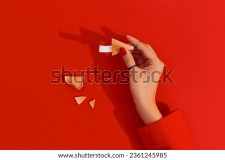 Women hands with manicure holding fortune cookie on red background. Blank paper for prediction words