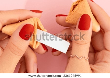 Women hands with manicure holding fortune cookie on pink background