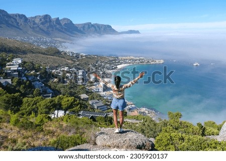 women with hands up at The Rock viewpoint in Cape Town over Campsbay, view over Camps Bay with fog over the ocean. fog coming in from the ocean at Camps Bay Cape Town South Africa