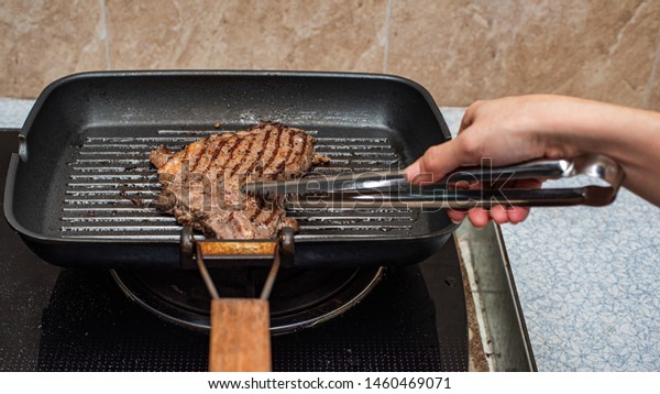 Women hands and The steak in the pan is grilled\
in the kitchen. Hot cooking seasoned meat steak in an oily pan.\
Juicy hot grilled