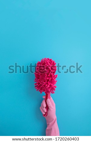 Women hands wearing pink glove holding red duster on blue background