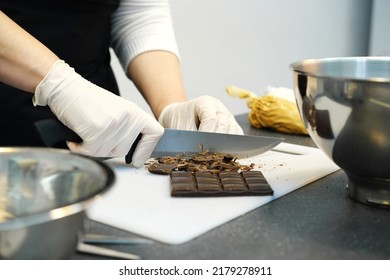 Women hands in white gloves cut a bar of dark chocolate with a knife. Confectioner prepares ingredients for dessert. Horizontal photo - Shutterstock ID 2179278911