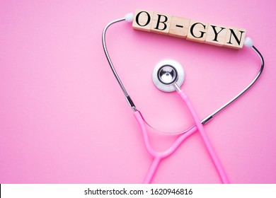 Women In Healthcare Concept. A Pink Strethoscope On A Pink Background, With Wooden Block Spelling OB-GYN, Or Obstetrics And Gynaecology