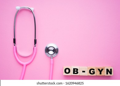 Women In Healthcare Concept. A Pink Strethoscope On A Pink Background, With Wooden Block Spelling OB-GYN, Or Obstetrics And Gynaecology