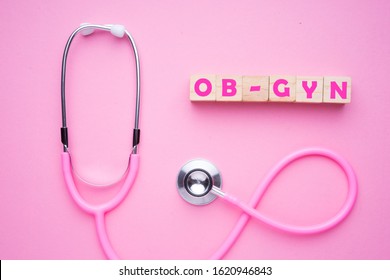 Women In Healthcare Concept. A Pink Strethoscope On A Pink Background, With Wooden Block Spelling OB-GYN, Or Obstetrics And Gynaecology