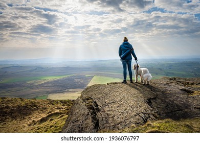 A women and her white dog enjoying the view of the Irish countryside after climbing Slemish Mountain in Northern Ireland