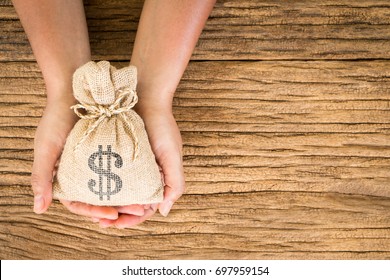 Women hold a money bag on the vintage wood background, a loan or saving money for future investment concept.