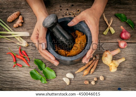 The Women hold pestle with mortar and spice red curry paste ingredient of thai popular food on rustic wooden background. Spices ingredients chilli ,pepper, garlic,galanga and kaffir lime leaves .
