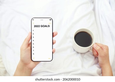 Women Holding 2022 Goals List On Mobile Phone And Cup Of Coffee, Setting New Year Goals And Resolutions