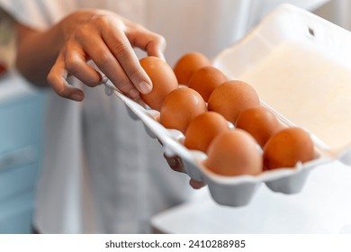 women with holding a cardboard egg box full of her eggs. the girl takes one chicken egg from a white box