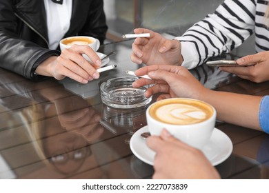 Women holding cigarettes over glass ashtray at table, closeup - Powered by Shutterstock