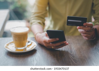 Women Are Holding Credit Card And Using Mobile Phone To Pay For Online Shopping In A Coffee Shop. Online Payment Concept.