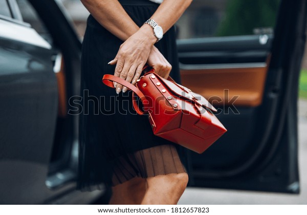 Women is holding\
handbag near luxury car