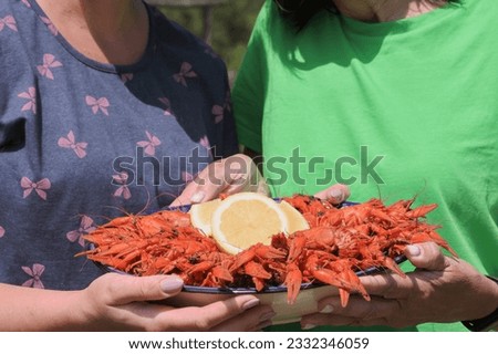 Women are holding a large dish with boiled crayfish in their hands. Garnished with lemon slices. Close-up.