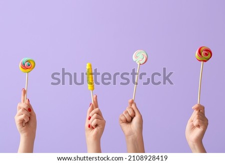 Women holding sweet lollipop on lilac background