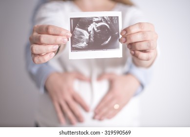Women holding ultrasound picture of her future daughter in the arms of her husband