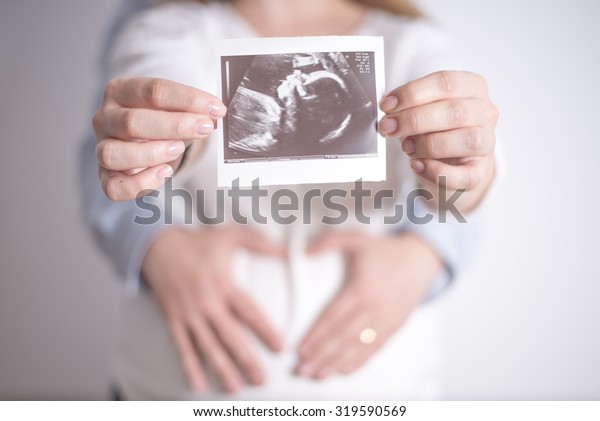 Women holding ultrasound picture of her\
future daughter in the arms of her\
husband