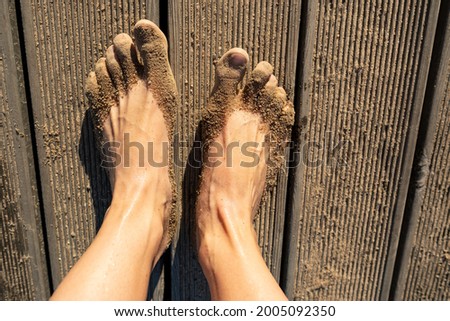 Women legs with sticky wet sand stand on a wooden pier, on the beach, on a sunny summer day. View from above. 
