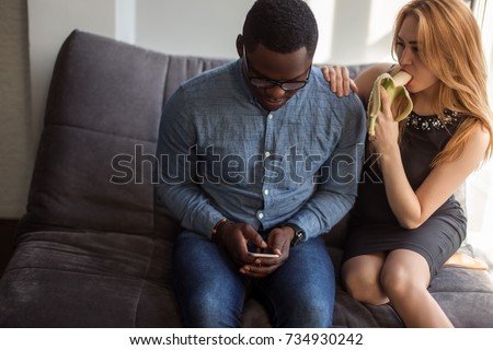 women looking at black man and eat banana while men sitting between them and using phone