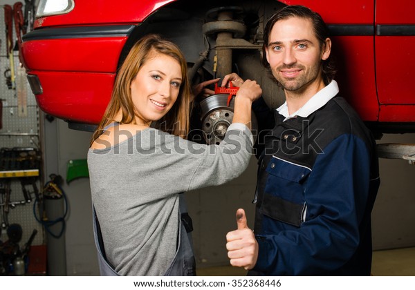 Women in male-dominated professions: Auto mechanic\
is happy with the success of a female trainee during maintenance of\
the brake disc of a car in a garage. Concept for the fact that more\
and more