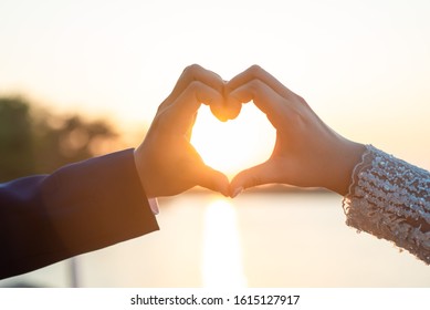 Women and men hands In the form of hearts against the sky through the sun's rays Hands in the form of love hearts