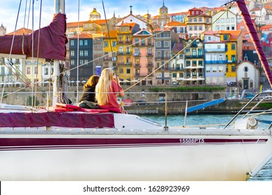 Women On A Private Yacht Drinking Wine Or Port Wine And Enjoying Sunset View In Porto, Portugal. Back View. Panorama Old City Porto At River Duoro. Oporto Panorama. Wine Degustation During Tour.