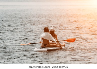 Women Paddleboard Sunset Ocean: Two women paddleboarding on a calm ocean at sunset. - Powered by Shutterstock