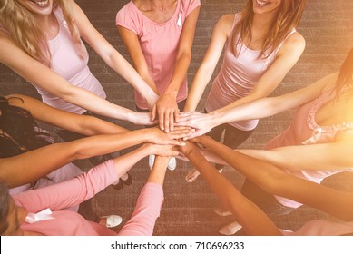 Women in pink outfits joining in a circle for breast cancer awareness against a dark wall