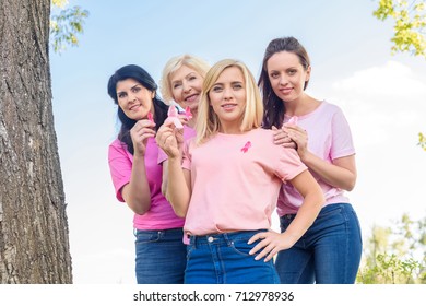 women in pink t-shirts holding breast cancer awareness ribbons and smiling at camera - Shutterstock ID 712978936