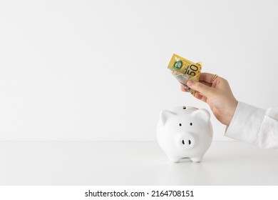 Women placing Australian dollar fifty 50 note into savings white piggy bank money box with copyspace