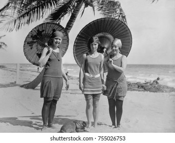 Women pose in bathing suits at an American east coast beach between 1910-1920. The younger woman in the center has bare legs, but the others wear stockings.